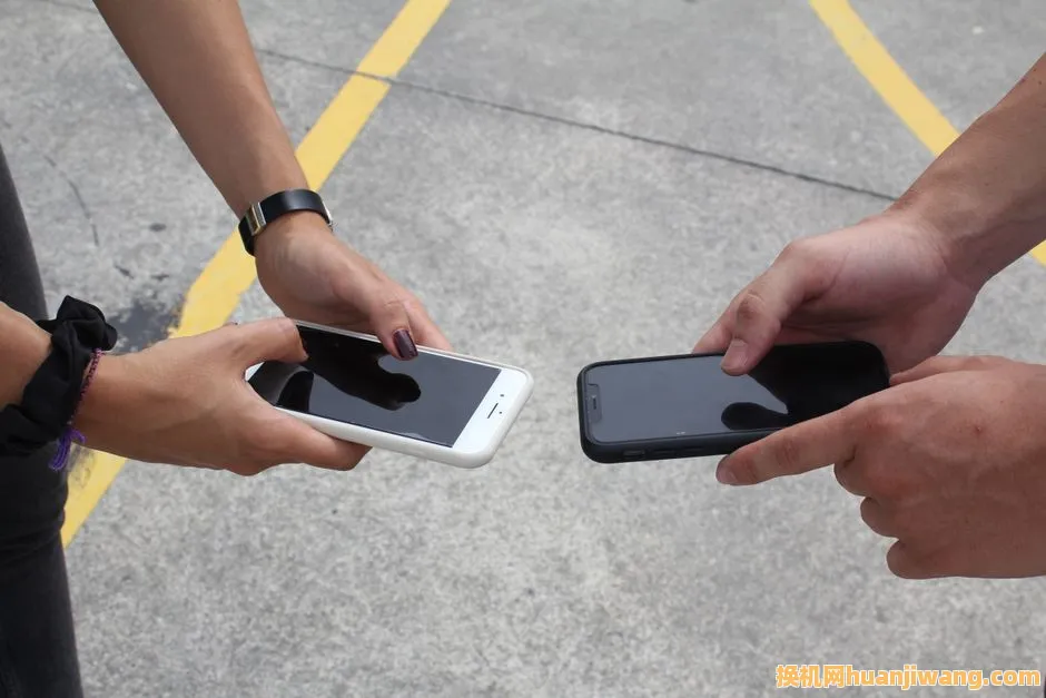 Two people exchanging or comparing smartphones in an outdoor setting, focusing on hands and technology.