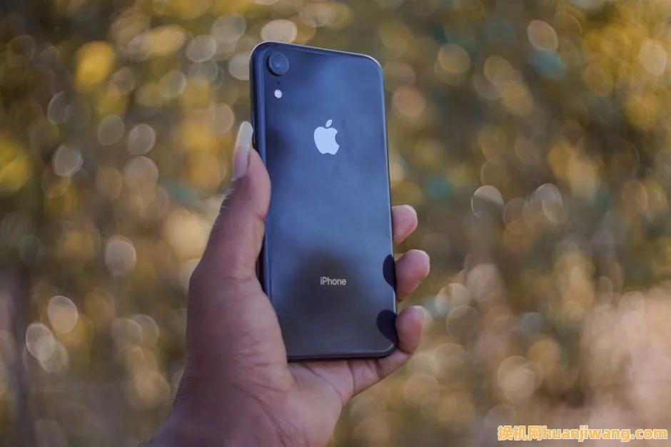 A close-up of a hand holding a smartphone with a blurred outdoor background.