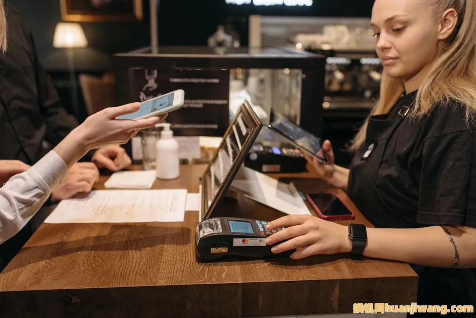 Customer using mobile phone for contactless payment at a coffee shop counter with a barista.