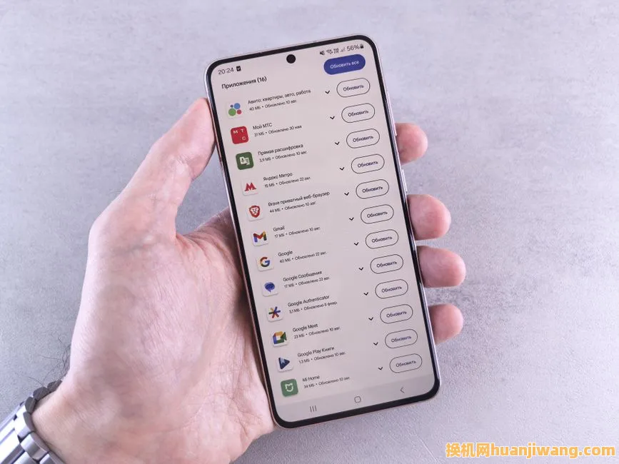 Close-up of a hand holding a smartphone displaying app updates on a light background.