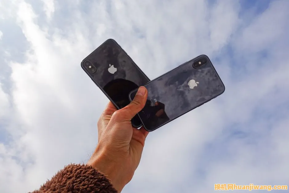 Close-up of a hand holding two smartphones against a cloudy sky, showcasing modern technology.