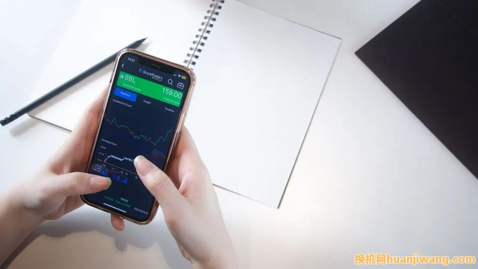 Close-up of hands using smartphone stock market app with notebook and pencil on desk.