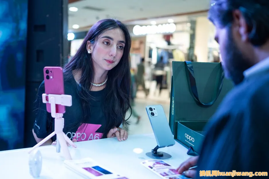 Woman at smartphone demo counter engages with salesperson in Islamabad retail setting.